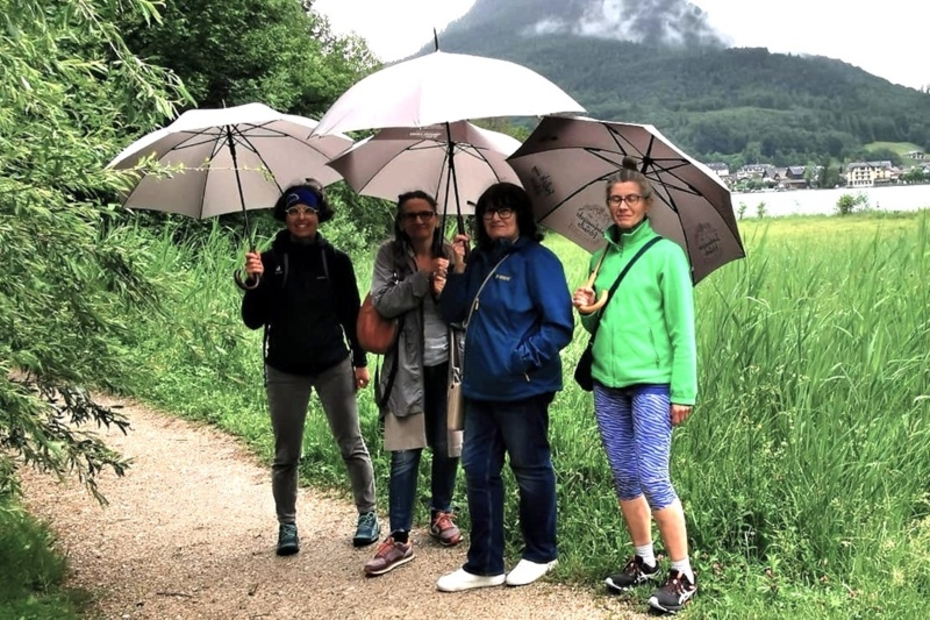 Vier Frauen stehen auf einem Wanderweg und haben Regenschirme aufgespannt. 