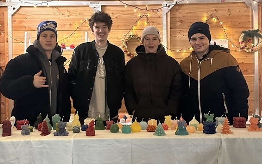 Vier Schüler stehen in einem Weihnachtsstand und verkaufen Kerzen