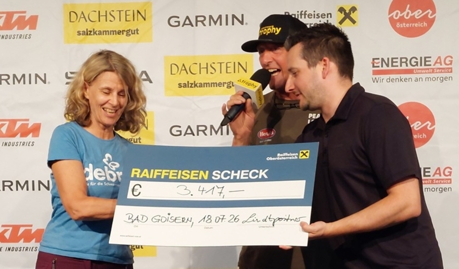 eine Frau und zwei Männer stehen auf einer Bühne und halten einen Spendenscheck