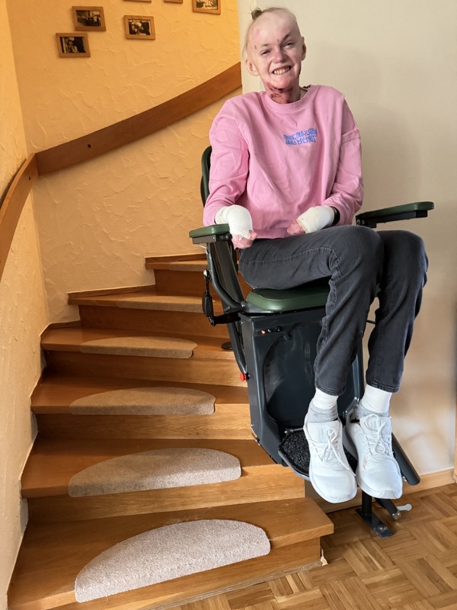 Junge Frau mit EB sitzt auf einem Treppenlift, im Hintergrund der Treppenaufgang