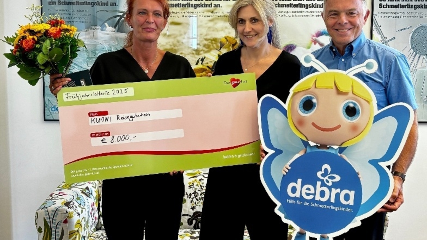 Zwei Frauen und ein Mann halten eine Pappfigur und einen Scheck