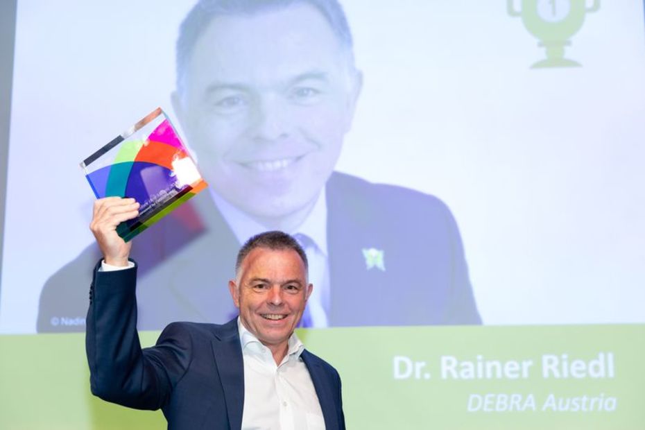 Rainer Riedl mit der Auszeichnung "Fundraiser des Jahres" in der Hand vor einer Leinwand