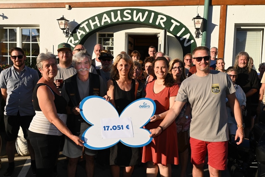 Mehrere Personen stehen vor einem Gasthaus mit einem Spendenscheck