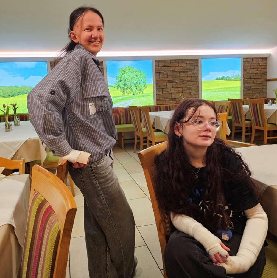 Eine junge Frau mit EB steht neben einer anderen, die im Rollstuhl sitzt