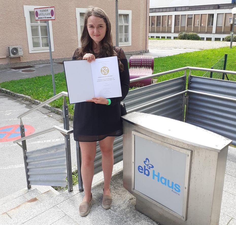 Junge Frau hält Dokument und steht am Eingang zum EB-Haus Austria