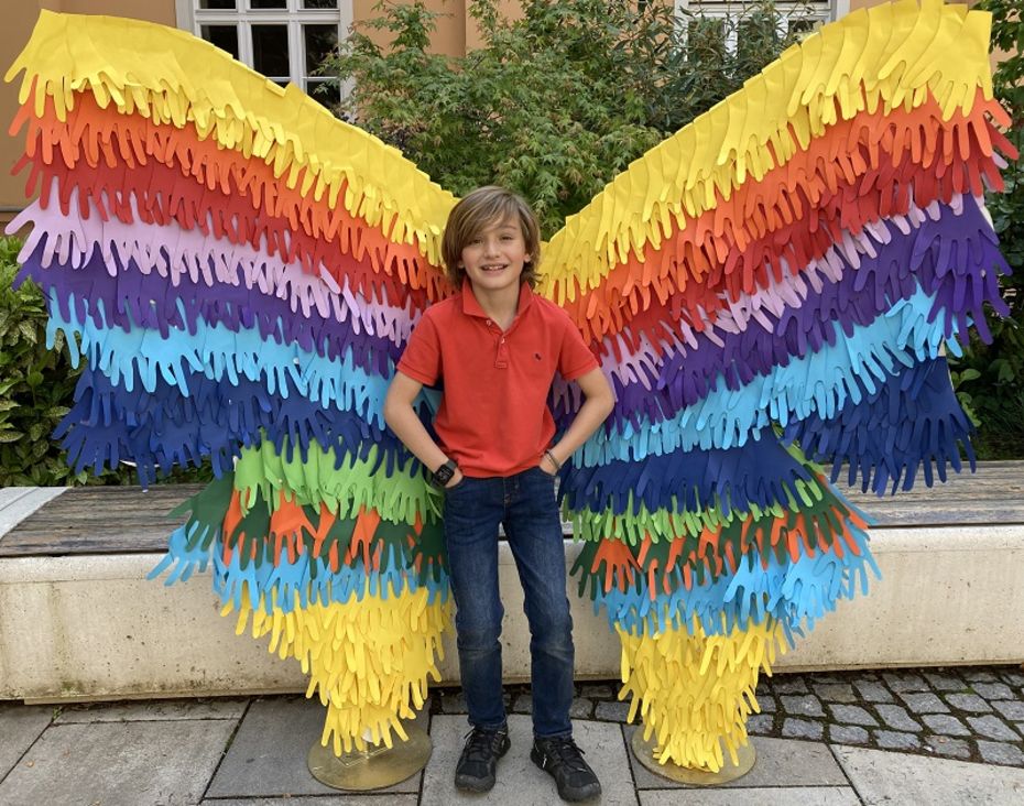 Schüler mit Riesenschmetterlingsflügeln aus gefalteten Papierschmetterlingen