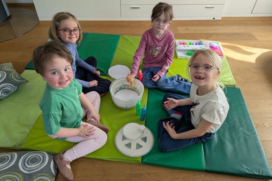 Vier Schmeterlingskinder zwischen 4 und 7 Jahren sitzen am Boden auf einer Decke und spielen