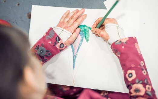 Schmetterlingskind mit Verbänden an den Armen zeichnet auf ein Blatt Papier