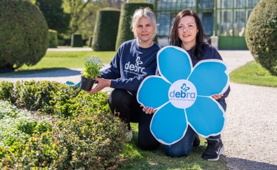 Zwei Frauen knieen in einer Wiese und halten eine große symbolische blaue Blüte