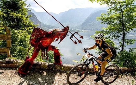 Ein als roter Teufel verkleideter Mann richtet symbolisch seinen Dreizack auf einen Mountainbiker