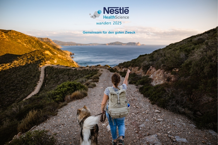 Eine Frau spaziert mit einem Hund auf einem Weg, im Hintergrund ist ein Gewässer.