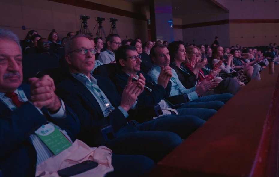 Viele Menschen sitzen in einem abgedunkelten Seminarsaal und schauen aufs Podium