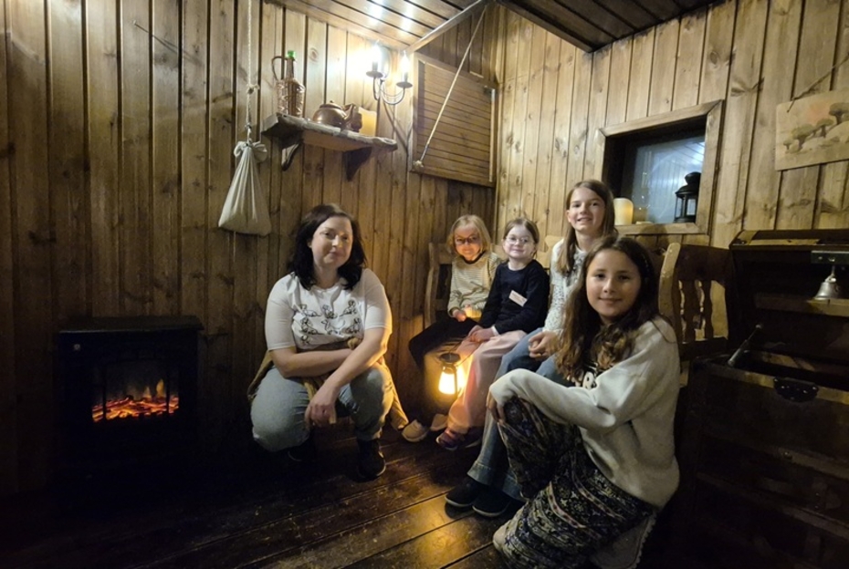 Eine Frau mit einer Gruppe von Mädchen mit EB sitzt in einem holzgetäfeltem dunklen Raum