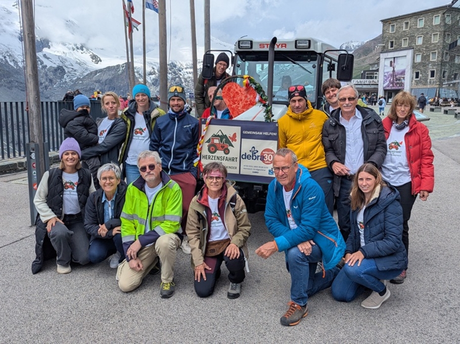 Gruppe von Menschen vor einem Traktor auf einer Bergeshöhe