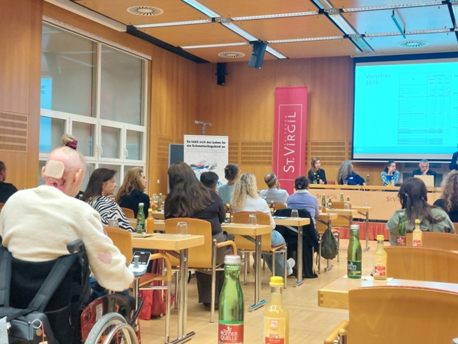 Mehrere Personen sitzen in einem Seminarraum, vorne ist ein Rednerpodium und eine Leinwand zu sehen