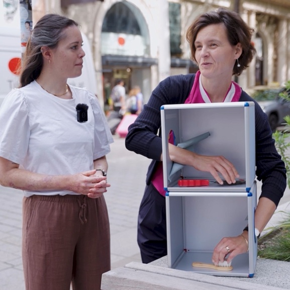 zwei Frauen stehen auf der Straße, eine davon greift mit ihren Händen in zwei Boxen
