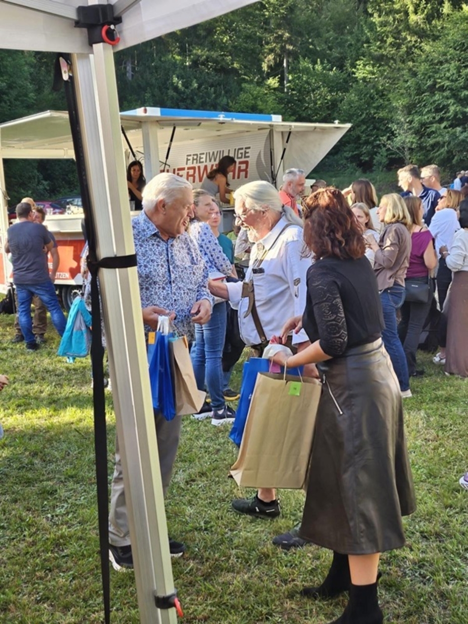 Menschen stehen auf einer Wiese, im Hintergrund ein Zelt der freiwilligen Feuerwehr