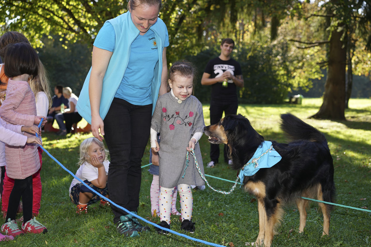 Schmetterlingskinder auf einer Wiese mit einem Therapiehund und dessen Besitzerin