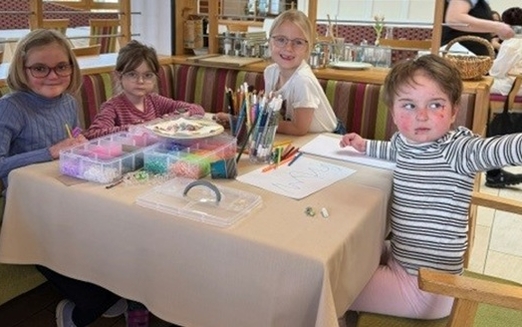 Schmetterlingskinder mit Verbänden an den Armen und Händen basteln an einem Tisch sitzend