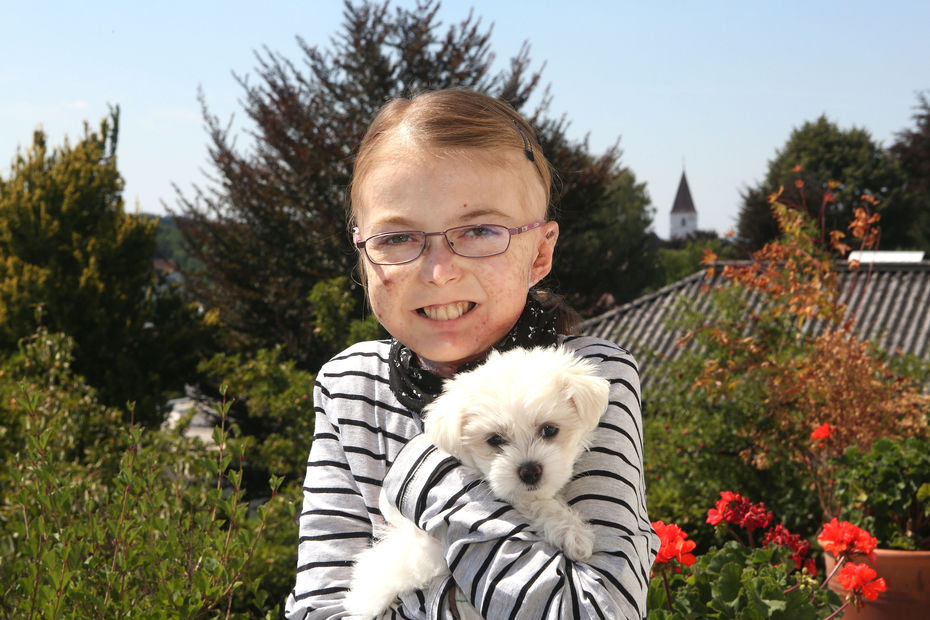 "Schmetterlingskind" Nina mit kleinem weißen Hund vor einer Blumenwiese