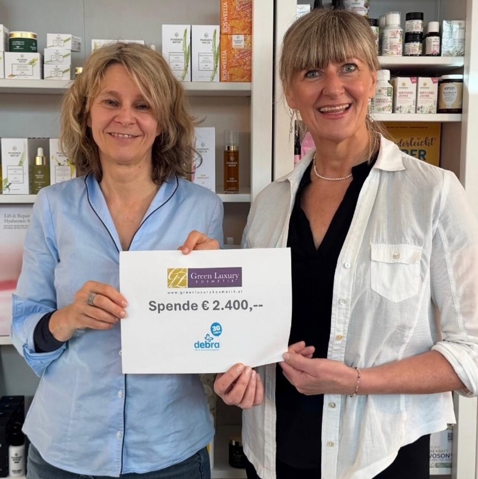 Zwei Frauen halten einen Spendenscheck und lächeln in die Kamera