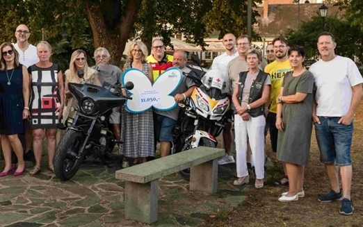 Mehrere Menschen stehen um ein Motorrad herum und halten einen Spendenscheck