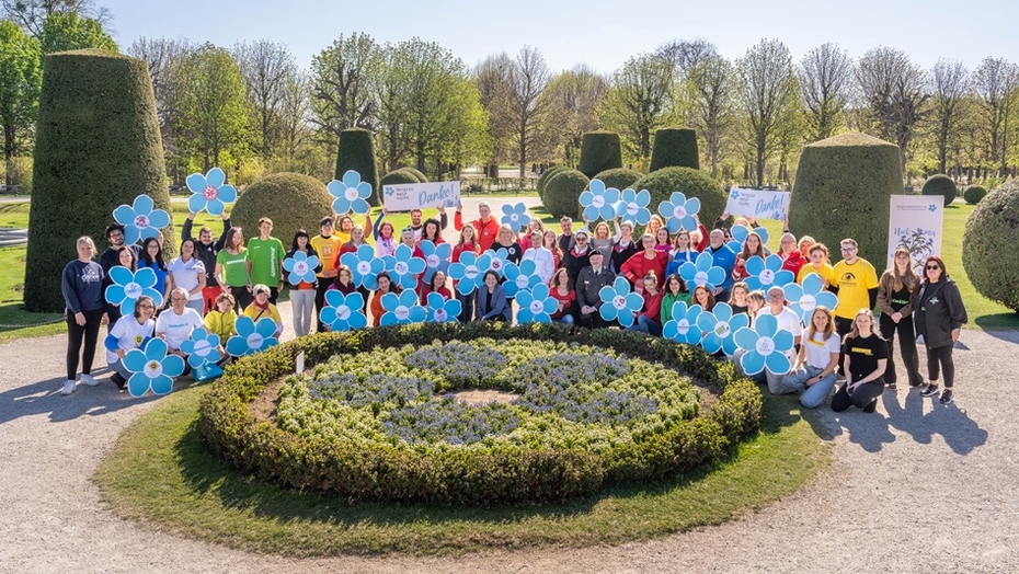 Eine Gruppe von Personen steht in einem Park, die einzelnen Menschen halten große symbolische Blüten