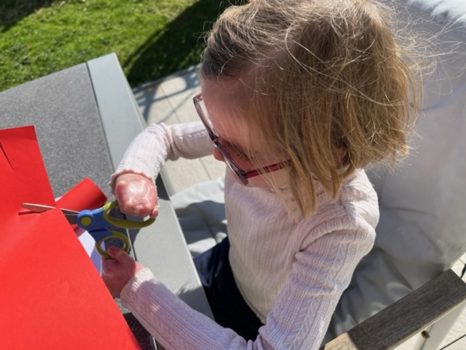 Schmetterlingskind schneidet rotes Bastelpapier mit einer Schere