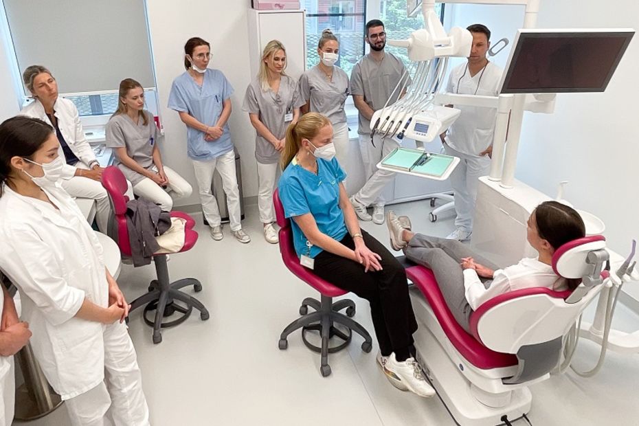 Zahnärztin mit Patientin am Behandlungsstuhl, im Hintergrund interessierte StudentInnen