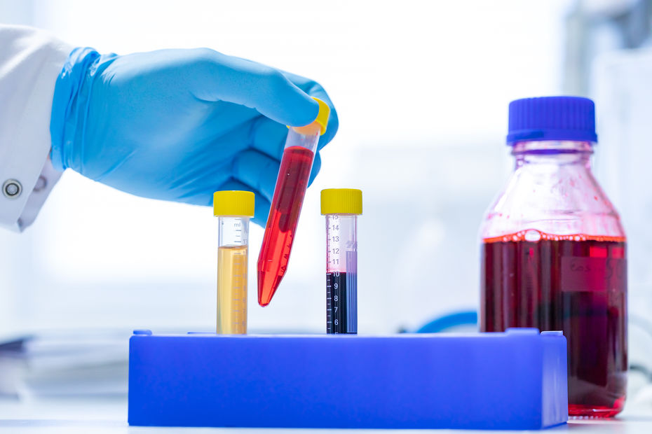 Laborszene mit Hand in Handschuh und Reagenzgläsern mit bunten Flüssigkeiten